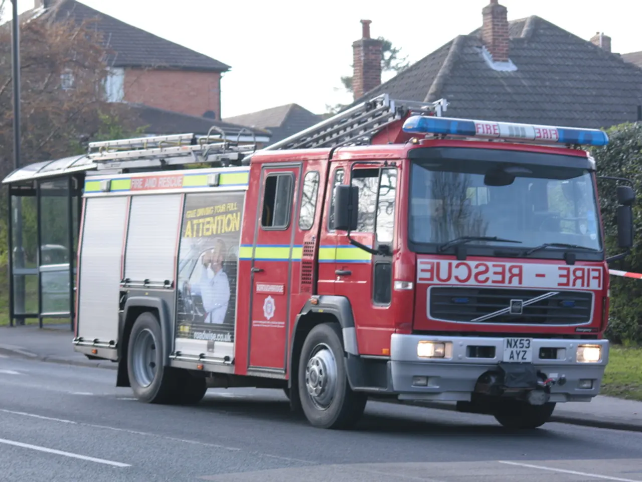 In this picture we can observe a red color vehicle on the road. There is a siren on the top of this...