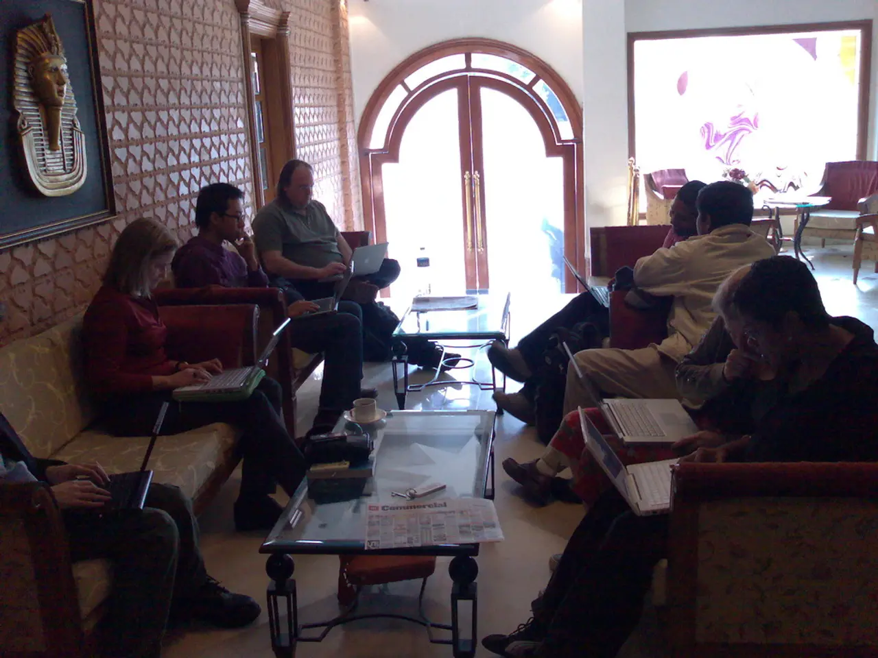 As we can see in the image there is a wall, door, screen, few people sitting on sofa and a table....