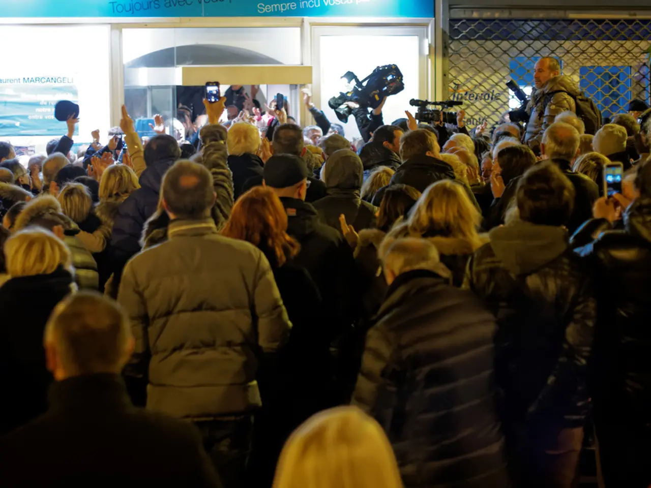 In the foreground of this image, there are people standing wearing coats few are holding cameras...