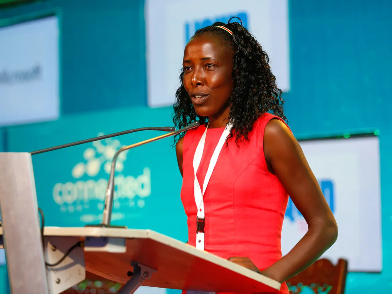 Here I can see a woman standing in front of the podium facing towards the left side and speaking on...