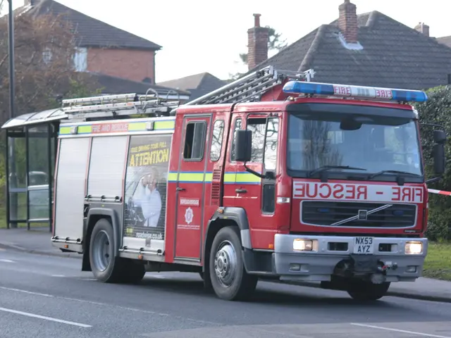 In this picture we can observe a red color vehicle on the road. There is a siren on the top of this...