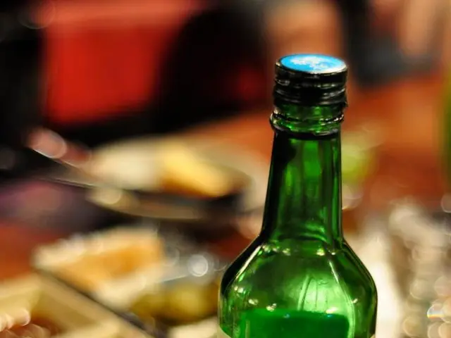 In this image there is a beer bottle with a label and a lie, there is a glass bowl on a table, in...