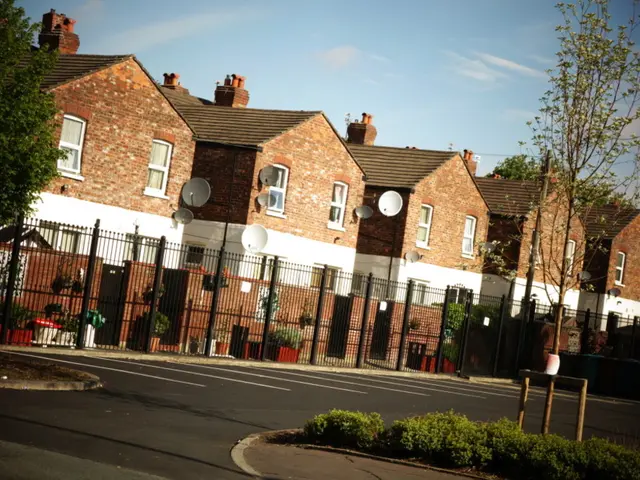 In this image I can see few buildings, windows, trees, railing, flower pots, road and the sky. I...