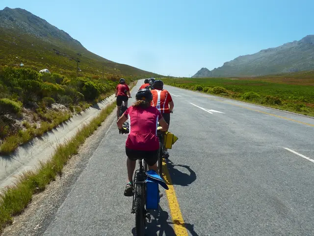 In this image we can see a group of people wearing the helmets cycling on the road. We can also see...